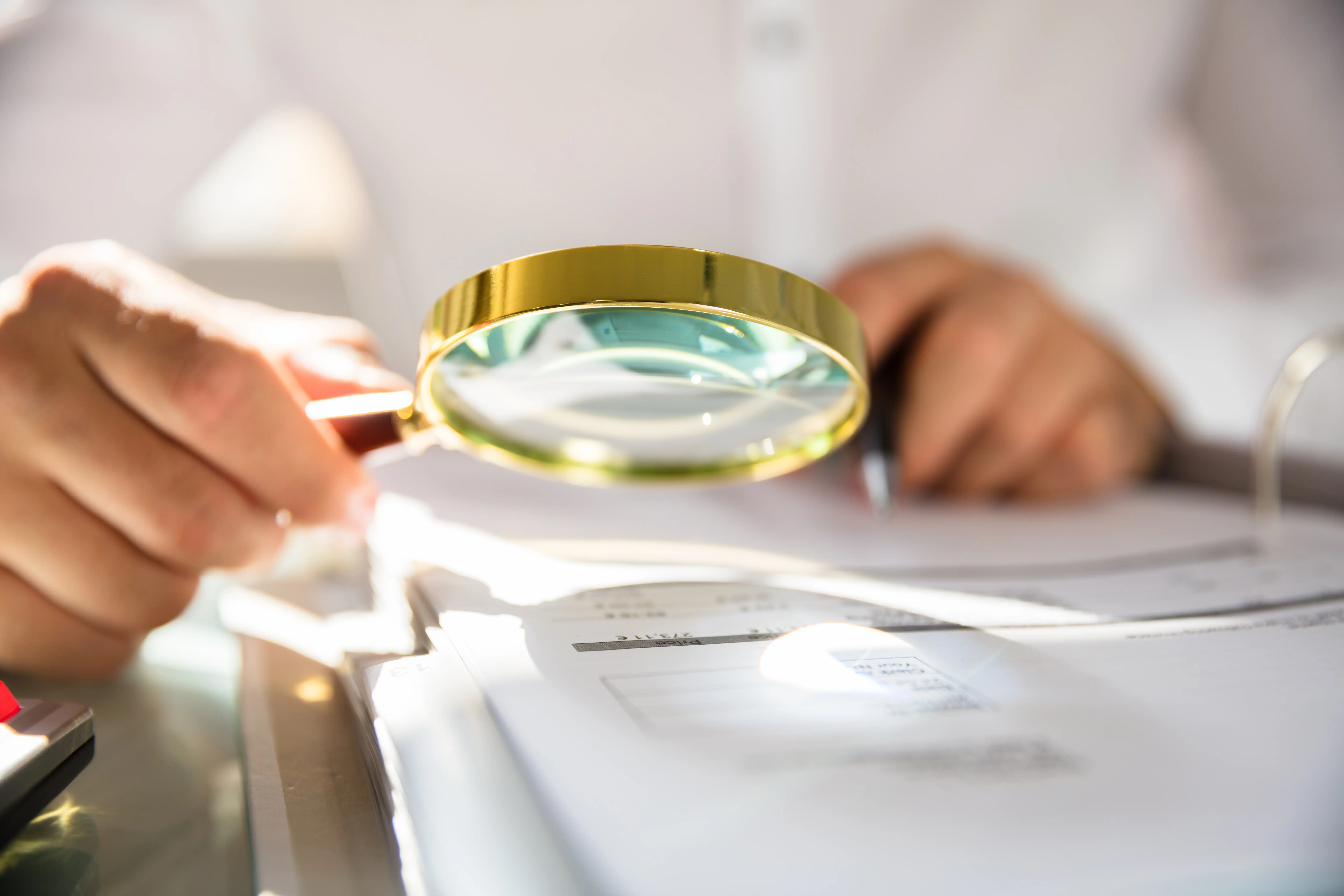 Businessman,Examining,Bill,Through,Magnifying,Glass,In,Office